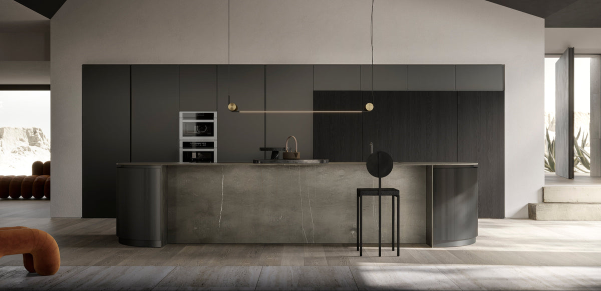A modern kitchen island and cabinetry set in a minimalist interior with a dark ceiling, light walls, and a concrete-look counter. A black bar stool stands in front of the island, and pendant lights hang above.