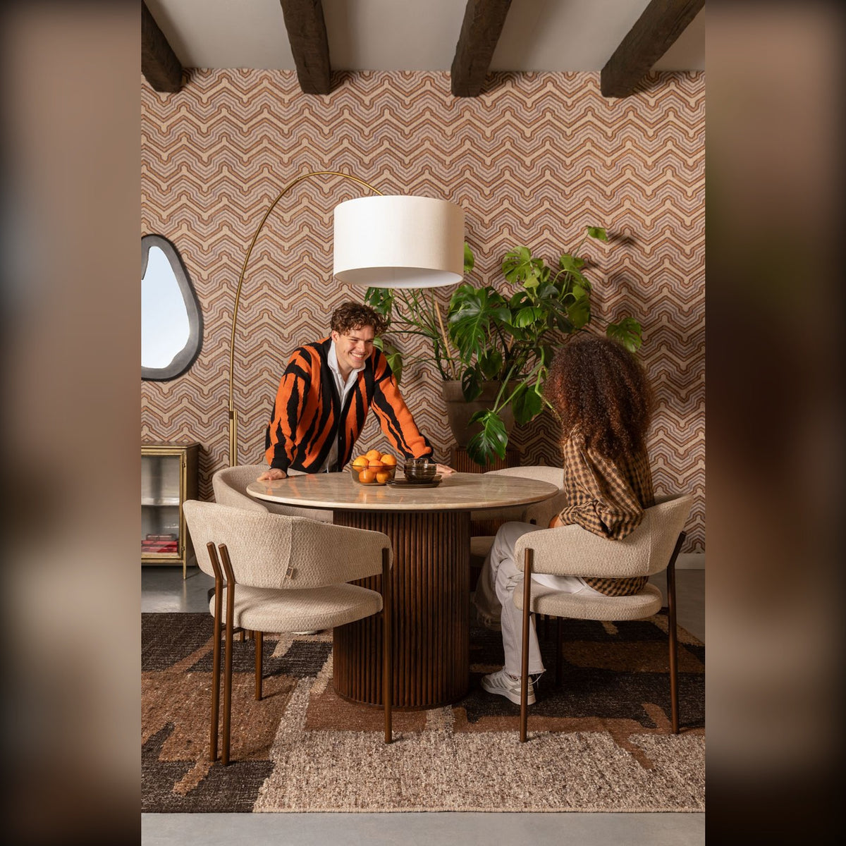 Dining Chair Naida Beige Domestica – Lifestyle – Couple Dining at a Round Table with Brick Wall and Arc Lamp